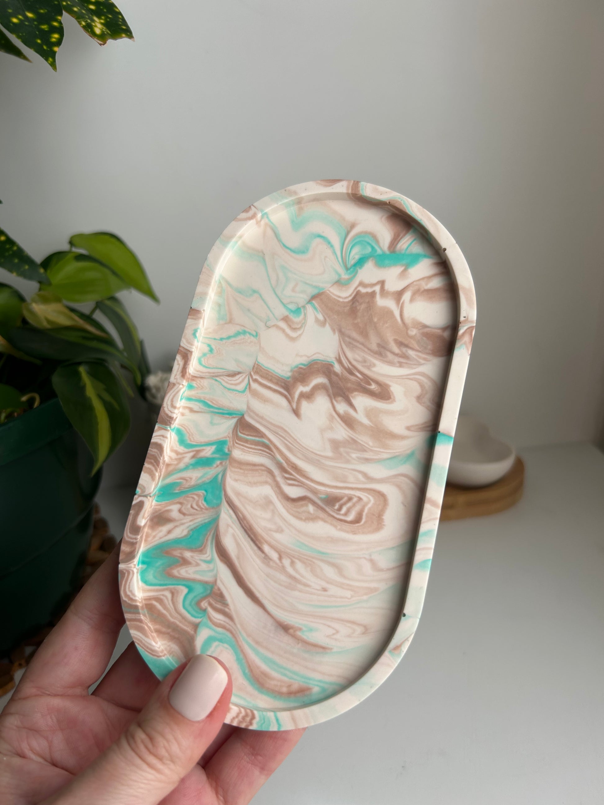 Marble-patterned oval tray held by a hand with a plant in the background
