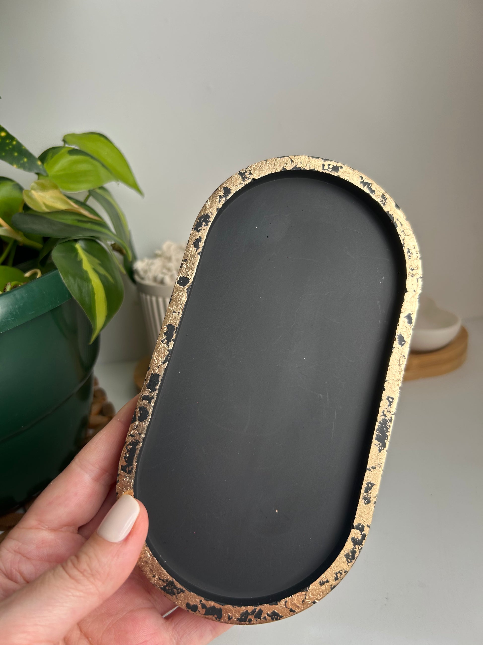 Hand holding a black tray with a textured gold rim against a neutral background