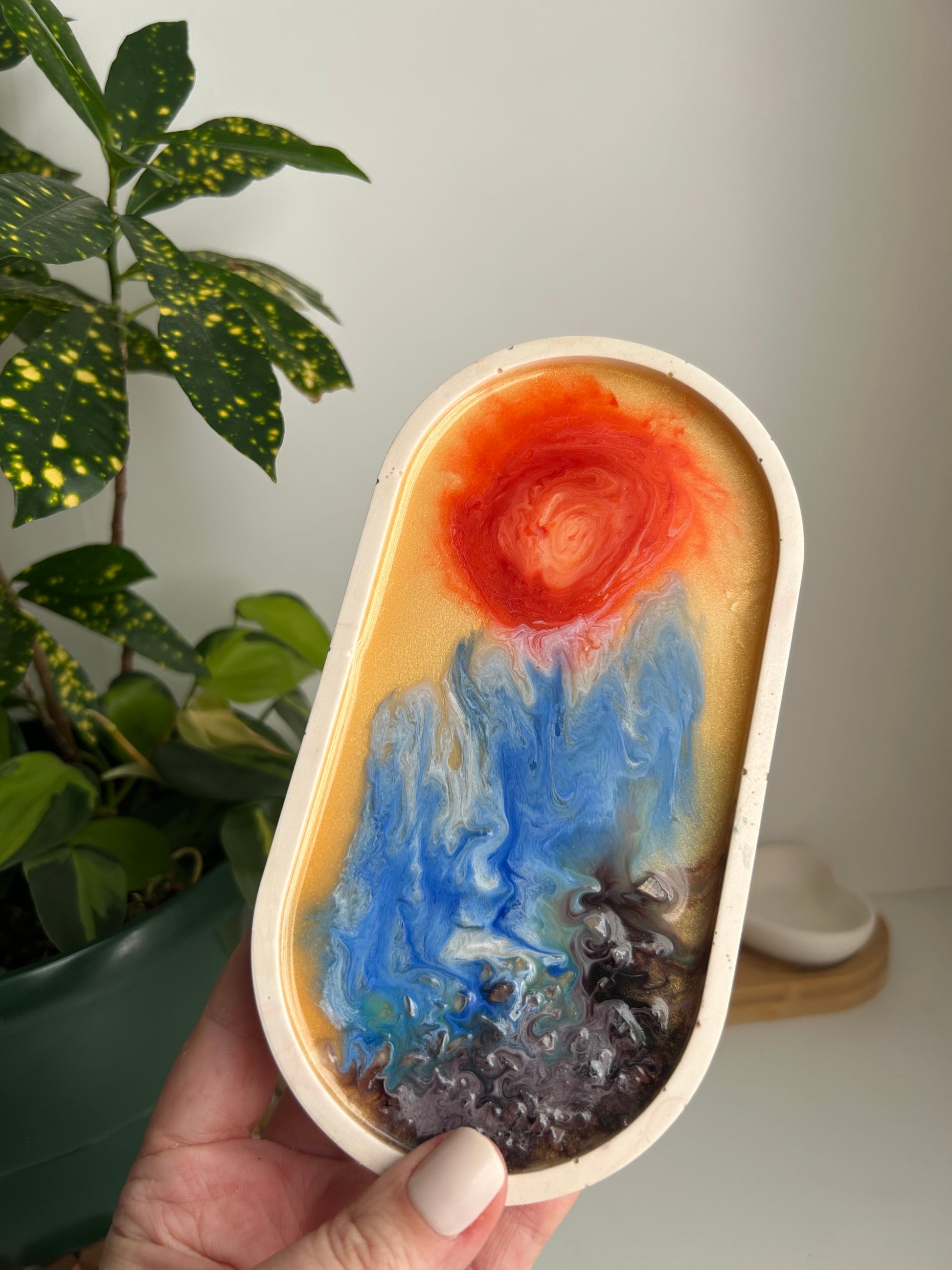 Hand holding a colorful abstract art piece with a plant in the background