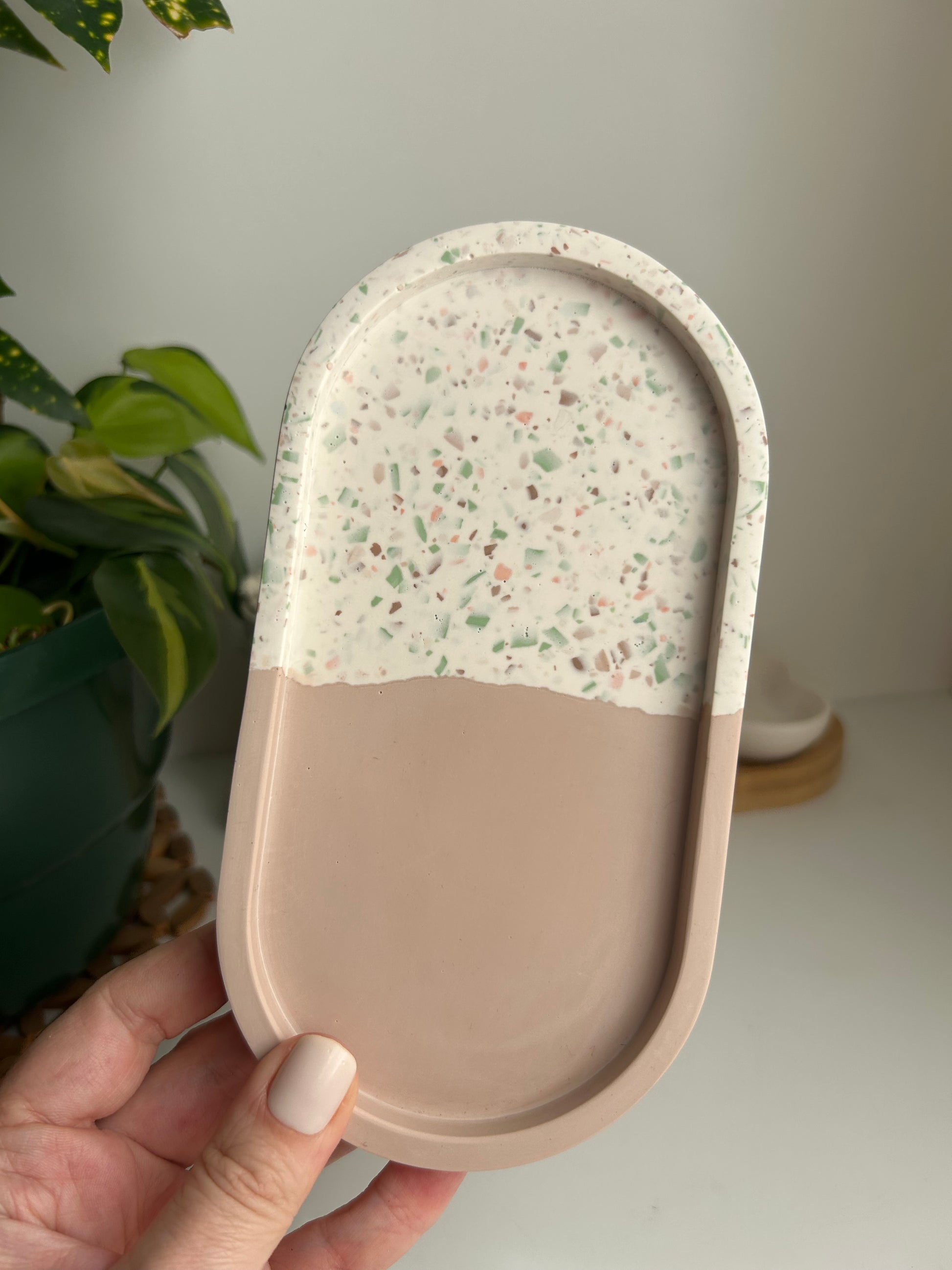 Hand holding a two-tone tray with one side having a speckled pattern and the other being solid beige.