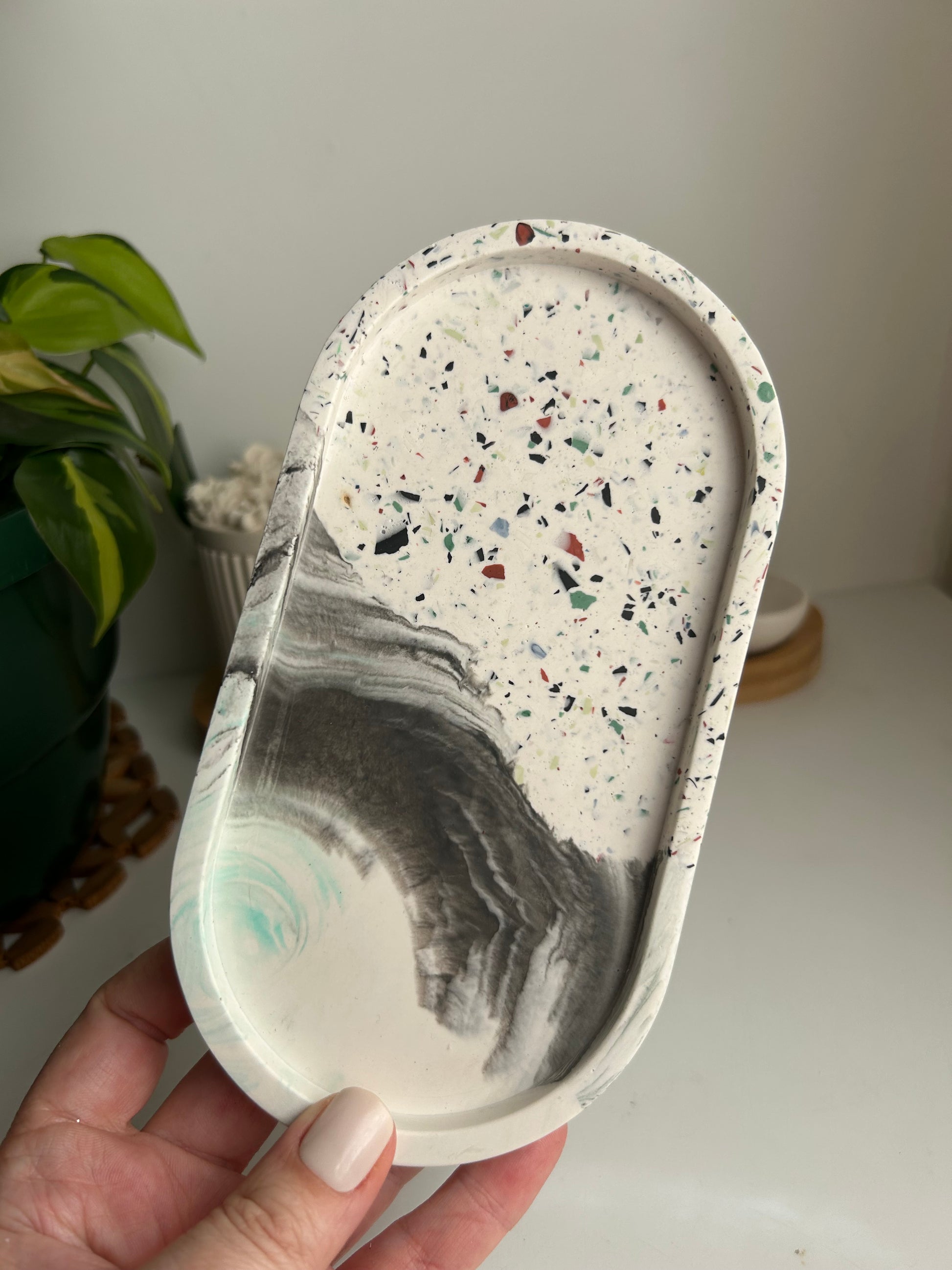 Hand holding a terrazzo-patterned tray with a eye of the storm design against a neutral background