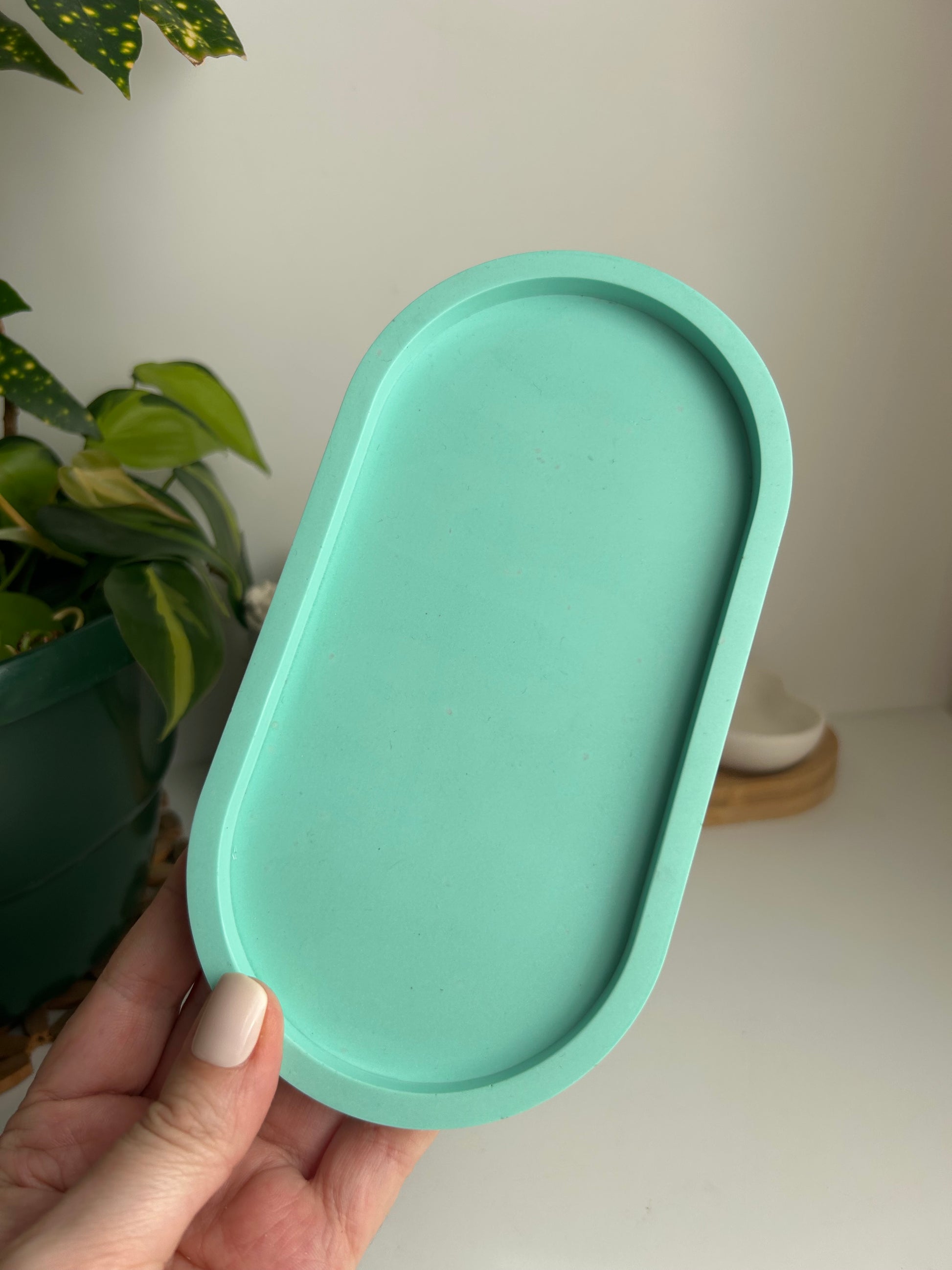 Hand holding a light sea foam green oval tray against a neutral background